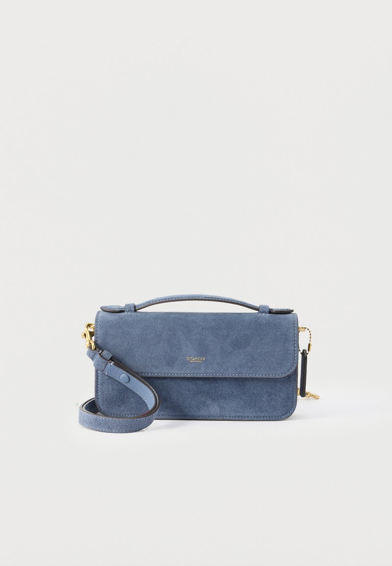 Ορθογώνια τσάντα από μπλε σουέντ με κορυφαία λαβή και αποσπώμενο λουρί ώμου, χρυσούς μεταλλικούς εξαρτήματα και μικρό ανάγλυφο λογότυπο στην εμπρόσθια πτερύγιο.