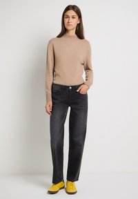 Suéter beige con un cuello alto, combinado con jeans negros de pierna recta y zapatillas amarillas. El conjunto presenta un diseño simple y casual.