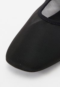 Scarpa nera in rete con punta quadrata e tomaia liscia e testurizzata. Presenta un profilo basso e un bordo in tessuto a contrasto attorno all'apertura.