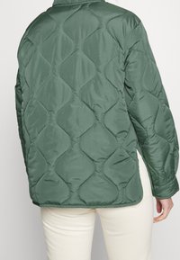 Giacca verde trapuntata con un motivo geometrico testurizzato, maniche lunghe e colletto rotondo, realizzata in un tessuto leggero e morbido.