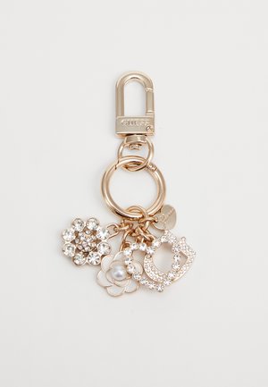 Porte-clés en or avec un fermoir à mousqueton, présentant trois charms : un orné de cristaux transparents, une fleur avec une perle et un design de lettre décoratif.