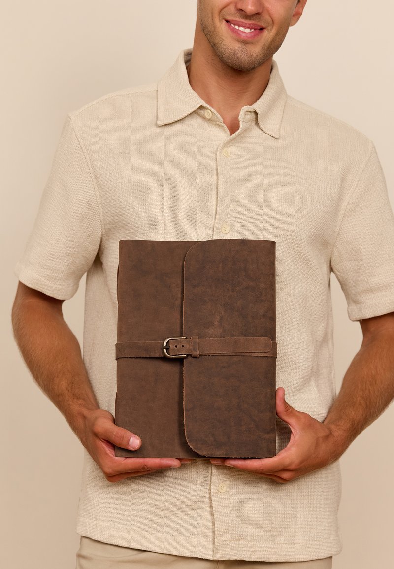 Hnedá kožená zložka s textúrovaným povrchom, vybavená pásikom a prackou na uzatváranie. Celkový dizajn je obdlžníkový s zaoblenými rohmi.