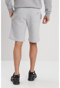 Pantalones cortos deportivos grises hechos de una mezcla de algodón, con un bolsillo trasero, cinturilla elástica y un corte relajado. Llevados con zapatillas deportivas negras.