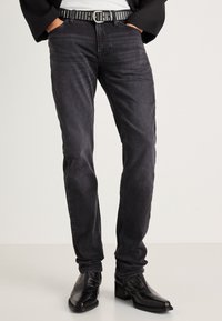 Mustad denim püksid slim-fit lõikega, millel on õrn tekstuur ja keskmise kõrgusega vö�ökoht. Aksessuaariks on studsiga must vöö ja stiilsed mustad saapad.