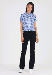 Camisa de cuadros azul y blanca de manga corta, combinada con jeans negros ajustados y zapatillas blancas. Diseño sencillo, corte ajustado.