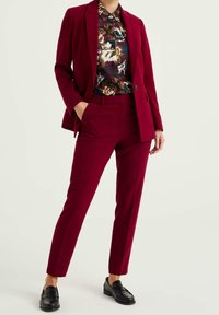 Burgundy kostym med skräddarsydd kavaj och slim fit byxor, parat med en flerfärgad blommönstrad skjorta. Svarta loafers fulländar looken.