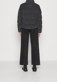 Svart kordflors pufferjacka med hög krage, med quiltade sektioner, tillsammans med vida svarta jeans och klumpiga svarta stövlar.