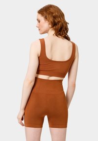Set di reggiseno sportivo marrone e pantaloni shorts a vita alta realizzati in tessuto morbido, con spalline larghe, design cropped e texture liscia.