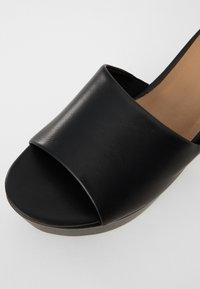 Black open-toe slide sandal made of smooth leather with a wide strap, featuring a flat sole and a minimalist design.