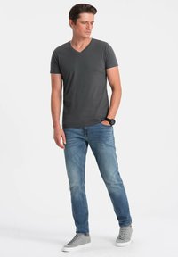 Šedé tričko s výstřihem do V v slim fit, spojené se světle modrými džíny. Tenisky jsou světle šedé s bílou podrážkou. Jednoduchý design a ležérní vzhled.