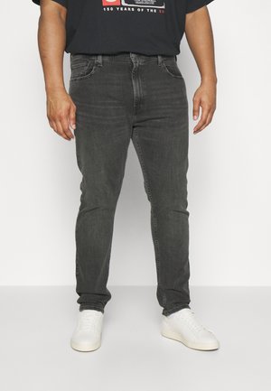 Graue Jeans aus Denim mit schmalem Schnitt, ausgestattet mit einem klassischen Fünf-Taschen-Design, kombiniert mit einem einfachen schwarzen T-Shirt und weißen Turnschuhen.