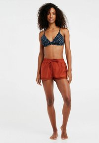 Top de bikini de lunares azul marino con bordes en forma de concha, combinado con pantalones cortos de baño de color óxido, con cordón en la cintura y detalle de encaje en el dobladillo.