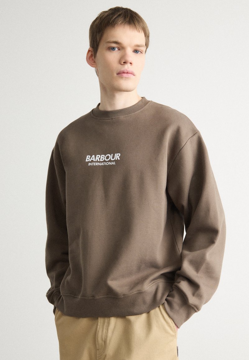 Sweatshirt marron avec un col rond, arborant le texte blanc "BARBOUR INTERNATIONAL" sur la poitrine. Fabriqué dans un tissu doux avec des poignets côtelés.