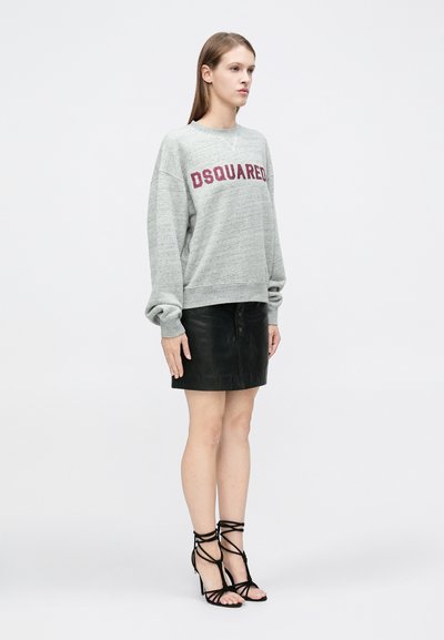 Pelēks sporta džemperis ar uzrakstu "DSQUARED" bordo krāsā, kombinēts ar melnu ādas mini svārku un melnām kurpēm ar siksniņām. Vienkāršs dizains, ikdienišķs izskats.