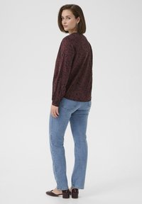Maroon bloemenpatroon lange mouwen top, gecombineerd met lichtblauwe rechte jeans. Model draagt bordeauxrode sleehakken. Zachte textuur, comfortabele pasvorm.