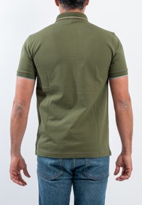 Polo shirt verde oliva a maniche corte, con colletto a bottoni e dettagli azzurri alle maniche, abbinato a jeans blu.