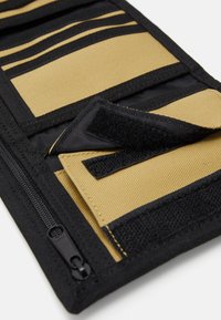 Black and tan wallet featuring textured fabric, multiple compartments, zip closure, and Velcro accents for secure storage.