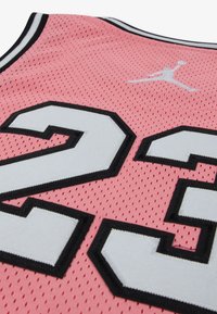 Ροζ μπασκετική φανέλα από διχτυωτό ύφασμα με μαύρο περίγραμμα, μεγάλο λευκό αριθμό "23" και λευκό λογότυπο Jumpman στο πίσω μέρος.