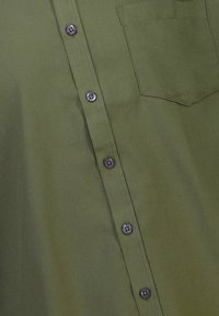 Camisa de botones verde oliva con una tela texturizada, con botones negros y un bolsillo en el pecho. Diseño simple sin patrones.