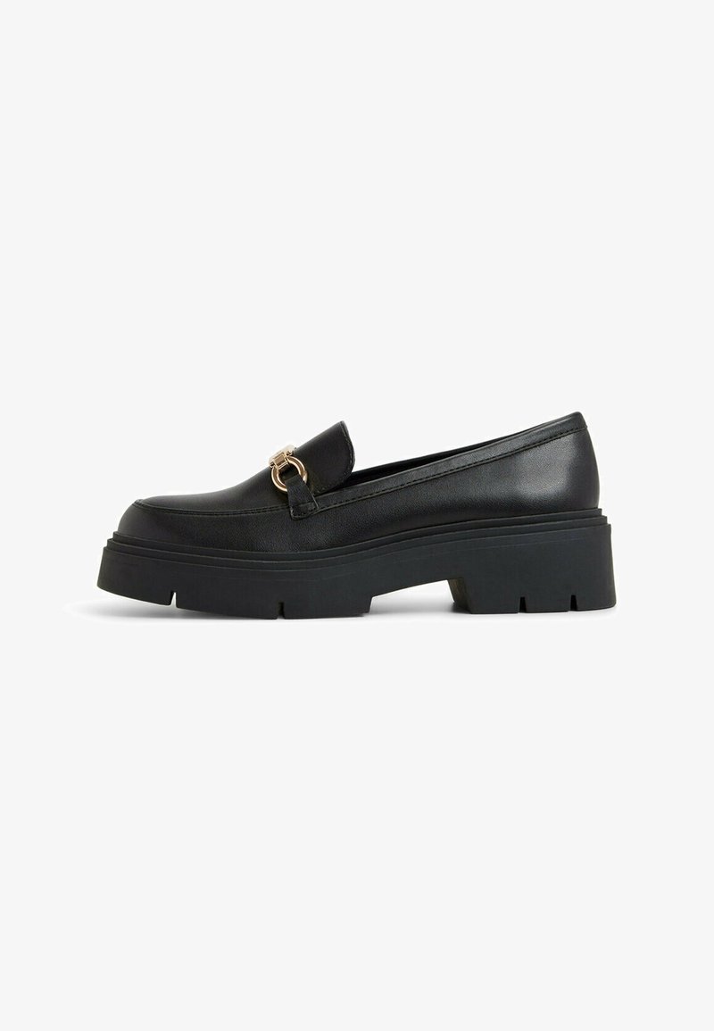 Black leather loafers with a chunky rubber sole, featuring a decorative gold hardware accent on the front. Smooth texture and streamlined design.