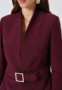 Bordeaux gepersonaliseerde blazer met een diepe V-hals en gestructureerde schouders. Voorzien van een brede stoffen riem met een gouden vierkante gesp.
