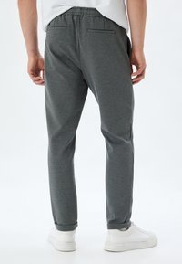 Pantaloni della tuta grigi con una finitura texturizzata, dotati di una vita elasticizzata, gambe affusolate e orli risvoltati, abbinati a sneaker bianche.