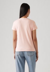 T-shirt rose clair à manches courtes avec un col rond, en tissu doux, associé à un jean bleu ample avec poches arrière.