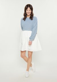 Pulover scurt cu dungi albastre și albe, asortat cu o fustă albă evazată, purtat cu adidași albi. Material neted cu o croială lejeră.