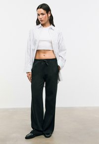Wit gestreepte blouse over een witte crop top, gecombineerd met zwarte sweatpants met trekkoord en zwarte platte schoenen. Glad materiaal, ontspannen pasvorm.