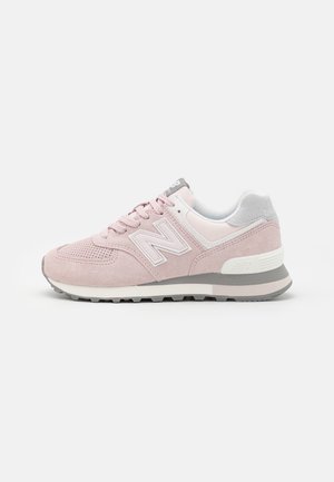 Różowo-szary but sportowy New Balance zamszowy i siateczkowy, sznurowany z przodu, z amortyzowaną podeszwą, widoczny z boku na białym tle.