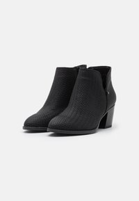 Bottes noires à la cheville avec une texture tissée, une forme angulaire et un talon carré moyen. Comprend une fermeture éclair sur le côté et des accents en cuir lisse.