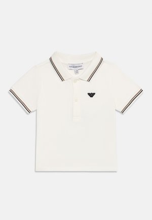 Polo para niño pequeño blanco con ribete de rayas negras y marrones en el cuello y las mangas, tapeta con botones, y logo de águila negra en el lado izquierdo del pecho.