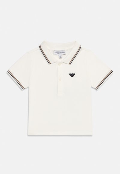 Λευκό παιδικό πόλο μπλουζάκι με ριγέ μαύρες και καφέ λεπτομέρειες στη λαιμόκοψη και τα μανίκια, κουμπότρυπες και μαύρο λογότυπο αετού στο αριστερό στήθος.