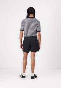 Polo à manches courtes avec un motif géométrique bleu marine et blanc, associé à un short noir. Poches arrière visibles et chaussures sombres.