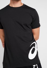 Black short-sleeve t-shirt made of cotton, featuring a large white logo on the lower left side and a crew neckline.