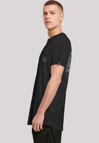 Black cotton t-shirt with a round neck, short sleeves, featuring intricate white graphic designs on the back and small details on the front.