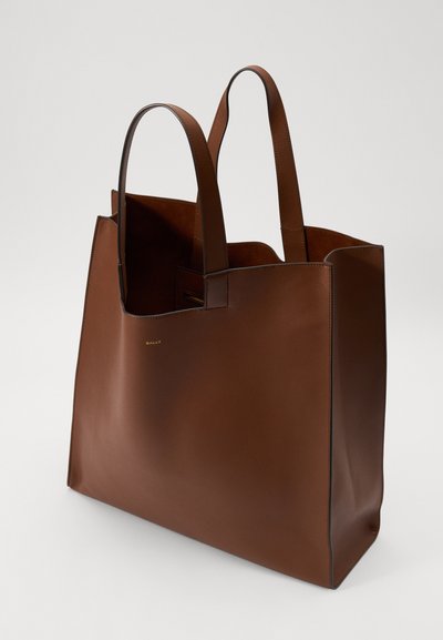 Barna bőr bevásárlótáska minimalista dizájnnal, sima textúrával és két masszív füllel. Az elején aranyozott, dombornyomott logó található.