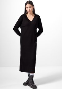 Robe noire en tricot côtelé avec un décolleté en V profond, des manches longues et une silhouette droite, associée à des bottes de combat noires à lacets.