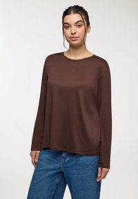 Brązowa, długosleeve koszula z okrągłym dekoltem, wykonana z miękkiego materiału. Połączona z jasnoniebieskimi dżinsami o luźnym kroju.