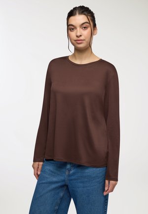 Camicia marrone a maniche lunghe con scollatura rotonda, realizzata in morbido tessuto. Abbinata a jeans in denim azzurro chiaro, dal taglio comodo.