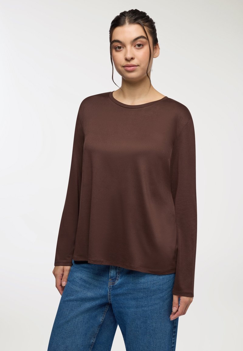 Brązowa, długosleeve koszula z okrągłym dekoltem, wykonana z miękkiego materiału. Połączona z jasnoniebieskimi dżinsami o luźnym kroju.