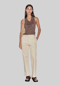 Bruine mouwloze top met een col, crèmekleurige op maat gemaakte broek en bruine sandalen met bandjes. De top heeft een geribbeld patroon en een getailleerde silhoeet.