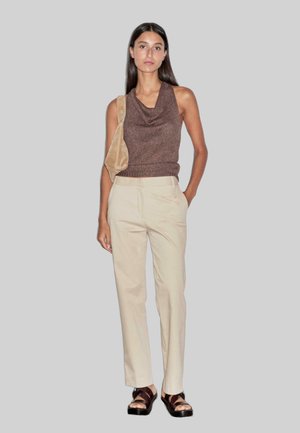 Bruine mouwloze top met een col, crèmekleurige op maat gemaakte broek en bruine sandalen met bandjes. De top heeft een geribbeld patroon en een getailleerde silhoeet.