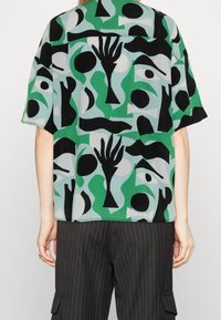 Blouse verte à manches courtes avec des motifs abstraits noirs et blancs. Tissu léger avec une coupe décontractée, dotée d'un ourlet droit et d'une silhouette ample.