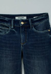 Tamno plave traperice s klasičnim dizajnom pet džepova, zlatnim dugmetima i bež šavovima. Na etiketi stoji "Salsa Jeans Faith."