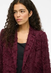Bordeaux strukturovaný blazer s třepeným detailem, s jedním knoflíkem a klopovými límci, nošený přes černý top.