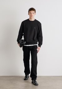 Schwarzer Hoodie und Hose, aus Baumwollmaterial, lockere Passform, weißes Shirt darunter, kombiniert mit schwarzen Schuhen, minimalistisches Design, keine sichtbaren Muster.