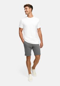 T-shirt blanc à manches courtes associé à un short gris retroussé et des baskets beiges. La tenue est décontractée et relaxée avec une texture lisse.