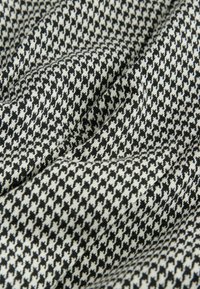 Čierno-biely houndstooth textil s jemným, textúrovaným povrchom. Vzor sa skladá z malých, striedajúcich sa čierno-bielych tvarov.