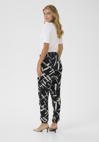 Pantaloni a righe in bianco e nero con vita elasticizzata, vestibilità rilassata e caviglie a coste, abbinati a una semplice maglietta bianca a maniche corte.